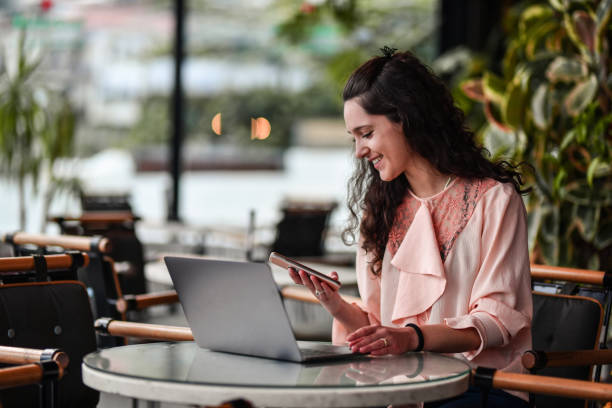 istock Beautiful Female Checking Smartphone While Using Laptop In Coffee Bar 1433373265