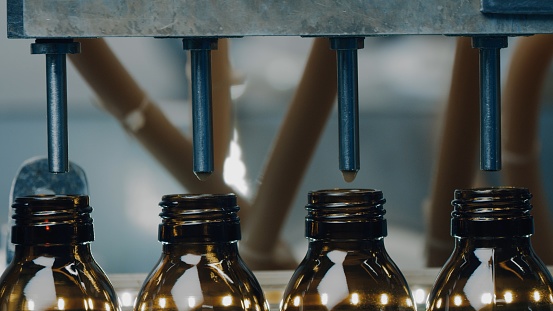 A row of glass bottles drive up and fill up with a liquid agent on a factory line. Manufacture drugs for medical supplies of pharmacy industry. Automatic bottling line. Close up