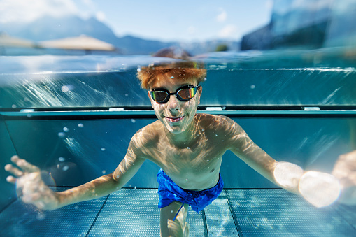 Teenage boy enjoying swimming underwater in the metal pool. The boy is swimming at the camera.\nFootage shot with Canon R5
