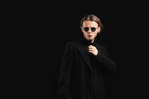 stylish man in sunglasses and a black coat on a black background, a handsome and brutal man with long hair.