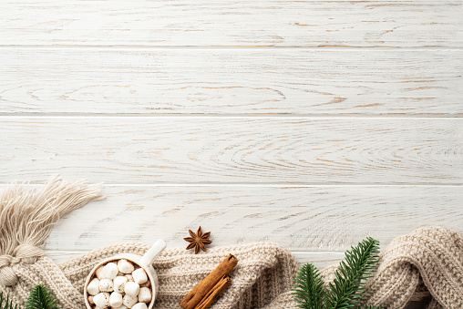 Christmas concept. Top view photo of pine branches mug of cocoa with marshmallow knitted plaid anise and cinnamon sticks on white wooden table background with empty space