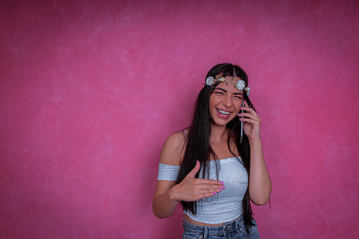 A studio shot of one cute and modern young woman with flowers in her hair, talking on the phone, smiling and gesticulating with her hands.