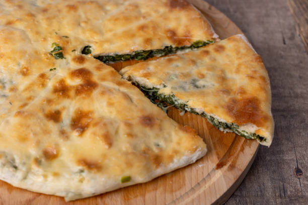 istock Pie with spinach, herbs and Suluguni cheese on a wooden board. The whole cake with the piece cut off. Traditional round flat cake with na 1433382995