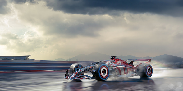 Close up of generic racing car with red an silver livery moving at high speed along a wet racing track under a stormy, overcast sky. With motion blur to the track, barrier and wheels.