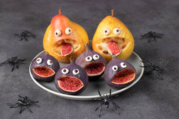 Spooky pear and fig monsters for Halloween party on gray background decorated with spiders and bats, Halloween Fruit Serving Idea stock photo
