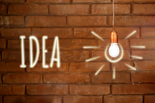 Idea and thought concept. A burning light bulb hangs against the background of a red brick wall