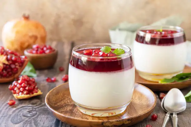 Photo of Winter delicious italian dessert panna cotta with pomegranate jelly and mint, homemade cuisine on a wooden background.