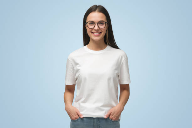 istock Young woman with hands in pockets, wearing blank white tshirt with copy space on blue background 1433385526