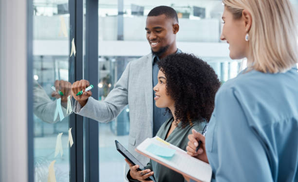 istock Teamwork, planning and collaboration strategy with a team working on glass wall with stick notes in an office. Diversity, writing and creative analytics workers in business meeting thinking of idea 1433387212