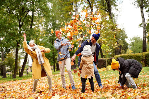 Happy Family of Five Have Fun in Autumn Golden Park, throwing leaves and laughing. Leisure Time Spending Outdoor. Active Lifestyle Concept.