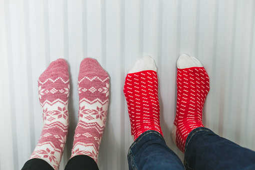 Color image depicting a couple warming their feet on the radiator while wearing cozy socks.