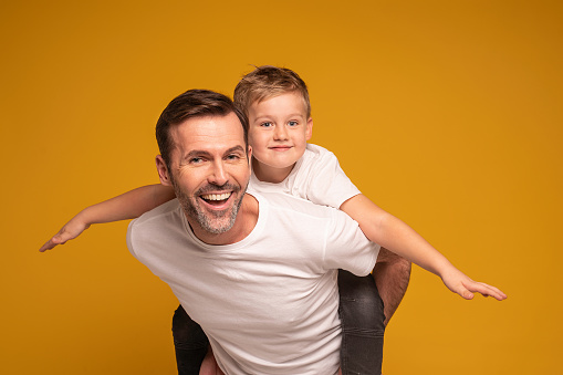 Portrait of dad playing with his son on color background. Real people emotions. Family lifestyle.