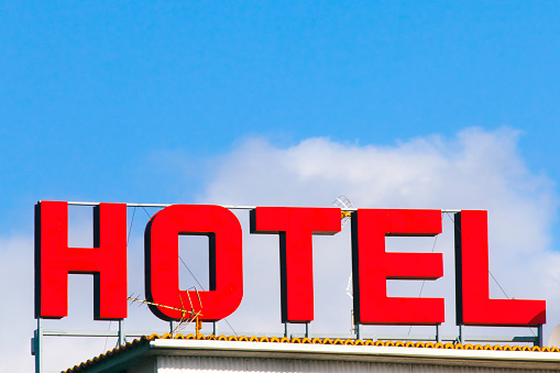 Large hotel sign on top of building, rooftop  , clear sky and clouds in the background.