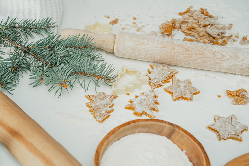 Partially blurred raw gingerbread cookies in shape of christmas trees and stars lie on kitchen countertop next to spruce branch, flour and rolling pin. Christmas pastries. Merry Christmas, New Year