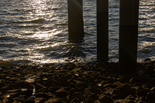 Posts under a pier and waves reflecting the sun during sunset