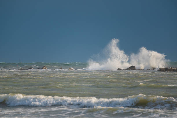 Big waves roll up on the beach. close parasol in bright Sunny day. White foaming waves and splashes.A hot summer day and high wave, seascape.Italy