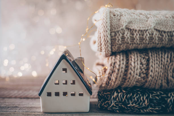 istock Stack of cozy winter knitted sweaters, ceramic house on a blurred background with bokeh. Warm Cozy Concept 1433403112