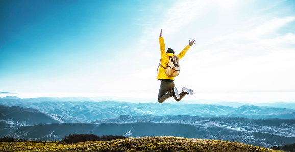 Happy man with open arms jumping on the top of mountain - Hiker with backpack celebrating success outdoor - People, success and sport concept