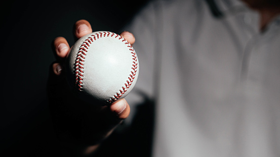 Selective focus of man holding baseball ball isolated on black background.