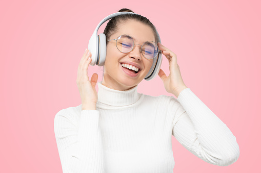 Favorite music. Young woman, moving to sound of favorite song through wireless headphones with eyes closed, isolated on pink studio background