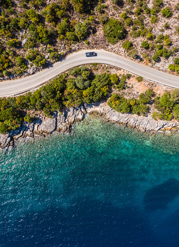 Aerial vertical shot of pickup truck moving by the curved road near sea tranquil waves on coast on Cephalonia Greek island. Transportation, traveling and nature concept.