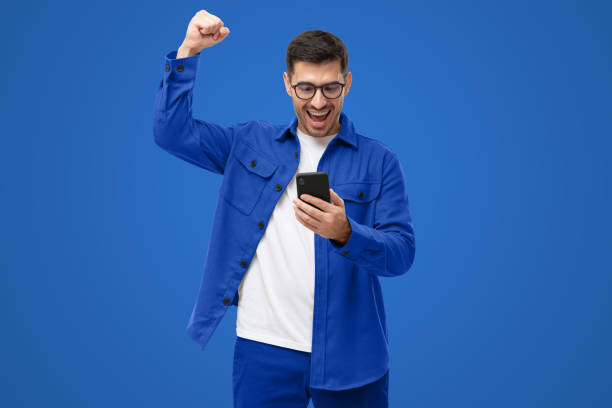 istock Happy young man in blue shirt looking at phone screen with victory expression 1433419989