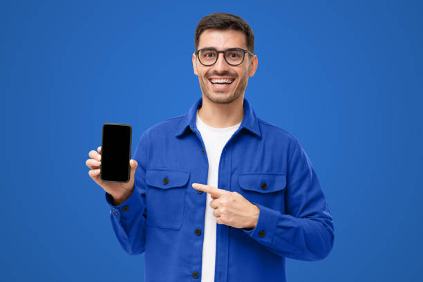 istock Happy laughing man showing with finger blank smartphone, smiling at camera, isolated on blue 1433420019