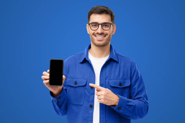 istock Handsome man in blue shirt presenting smart phone and pointing with finger at blank black screen 1433420027