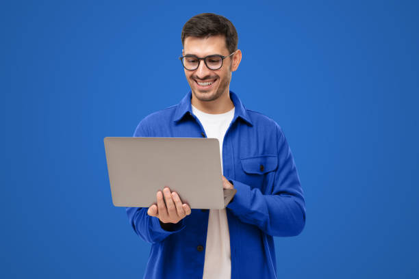 istock Happy man standing with opened laptop, browsing online or typing message, isolated on blue 1433420052