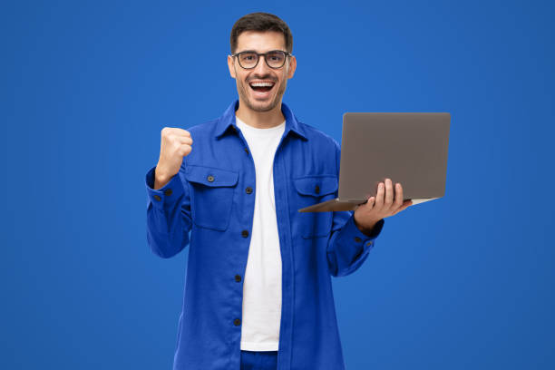 istock Happy young man in blue shirt looking at laptop screen with victory expression 1433420054