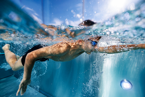 Teenage boy enjoying swimming underwater in the modern swimming pool. The boy is swimming freestyle.\nShot with Canon R5