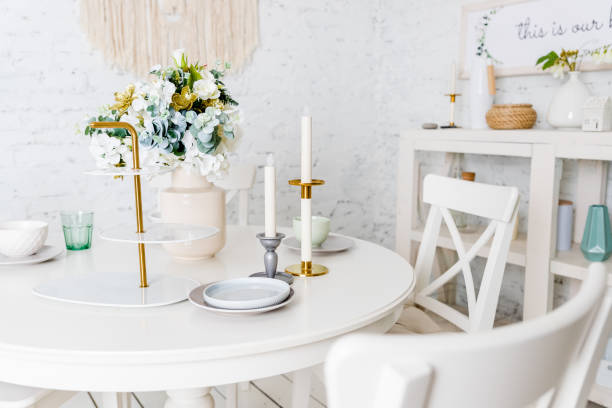 Stylish kitchen in white and brown wood. Style minimalism. Sink, table top, plants, pot, shelf for dishes. Bar stools, table. elegante cocina en blanco, colores pastel. estilo minimalista. jarrón con flores, mesa blanca, velas, vasos, platos, platos. interior moderno con muebles blancos, mesa, paredes de ladrillo. loft apartamento .bright cocina en el estilo de la provenza