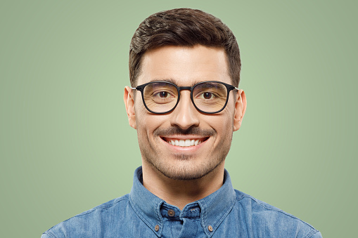 Eyewear fashion. Headshot portrait of handsome smiling man dressed in blue denim shirt and wearing eyeglasses, isolated on green background