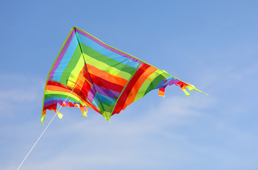 colorful kite flies high in the blue sky tied to a string