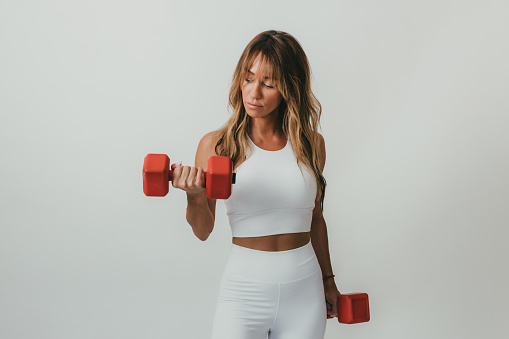 Portrait of a beautiful young woman exercising with red color dumbbells, studio shot in front of a white background