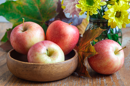 Autumn season or Thanksgiving holiday concept with apples in bowl, flowers and fall leaves on wooden table, horizontal, closeup