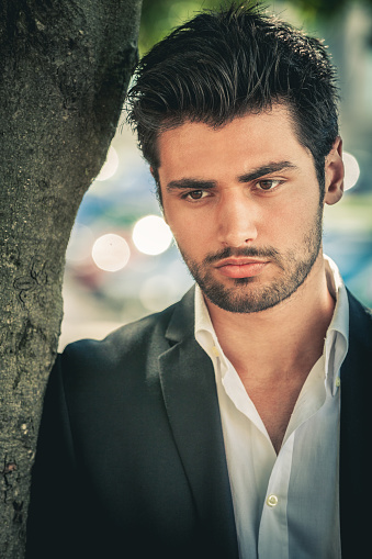 Portrait of handsome and attractive pensive man. Looking down. Dressing a white shirt and jacket. Trendy hair and beard.