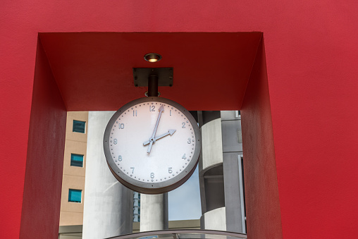 Hanging clock against a red wall by the city.