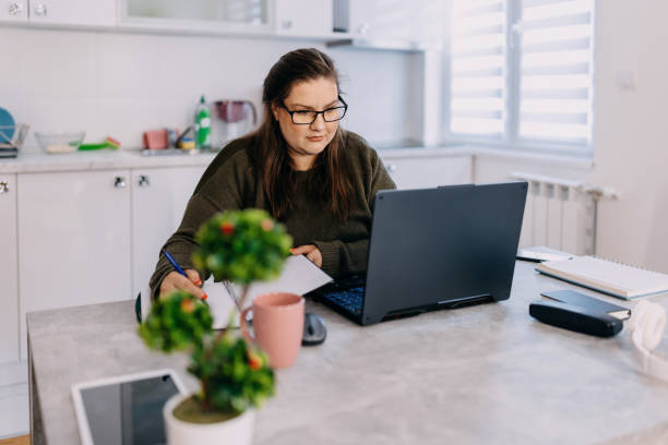 istock Concentrated woman looking at laptop and writing in note pad 1433445183