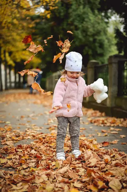 Photo of little girl  enjoying sunny autumn days in a city steet with fallen leaves.