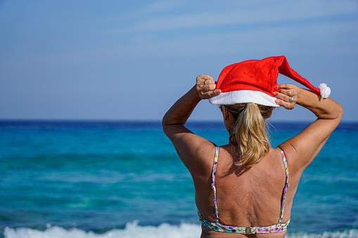 woman putting on a santa claus hat on the beach. Christmas holiday