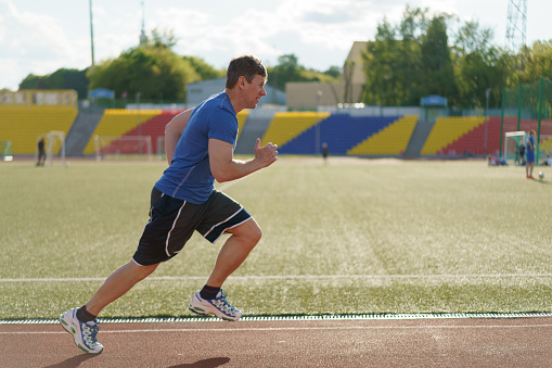 Handsome man trains at stadium in Moscow city. He put on a sports uniform and runs outdoors. in sunny summer day. He looks healthy. Concept of the active lifestyle. Time for jogging