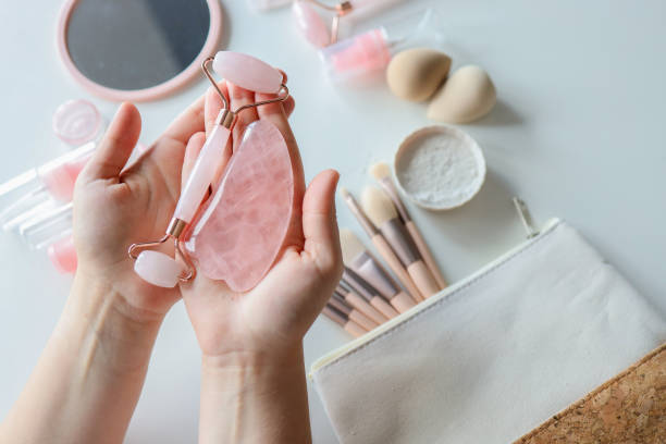 istock Woman holding gua sha tool and cosmetic over white table, top view 1433450440