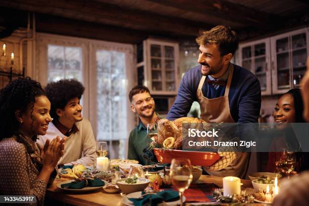 Young Happy Man Serving Thanksgiving Turkey To His Friends At Dining Table Stock Photo - Download Image Now