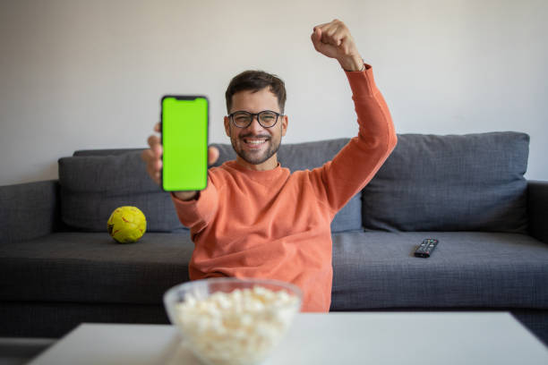 Excited man cheering while watching tv at home Handsome young man watching soccer match on TV at home online soccer free betting stock pictures, royalty-free photos & images