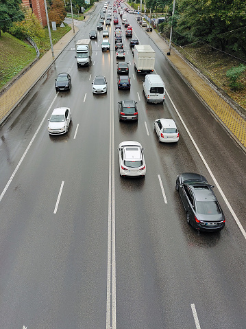 A variety of cars drive on an asphalt two-way road in perspective in the city. View from above