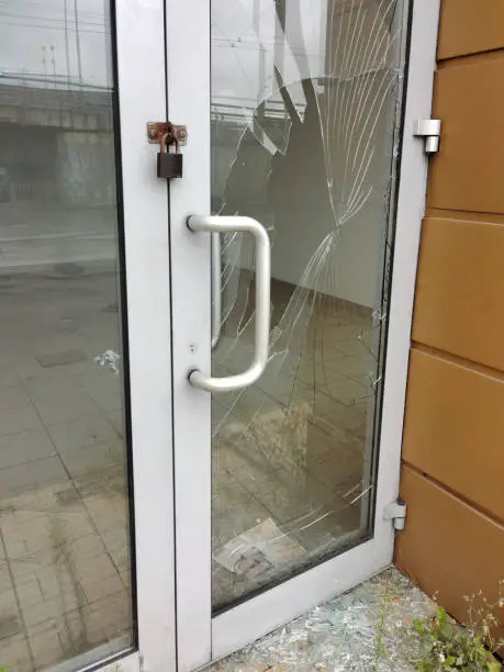 Photo of The glass of a store door broken by thieves or vandals with a padlock hanging from it