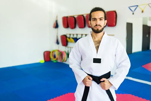 Portrait of a mid-adult man wearing a white kimono practicing karate against dark grunge background.