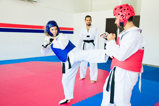 Strong young woman with a safety helmet sparring with a man fighter during a karate practice