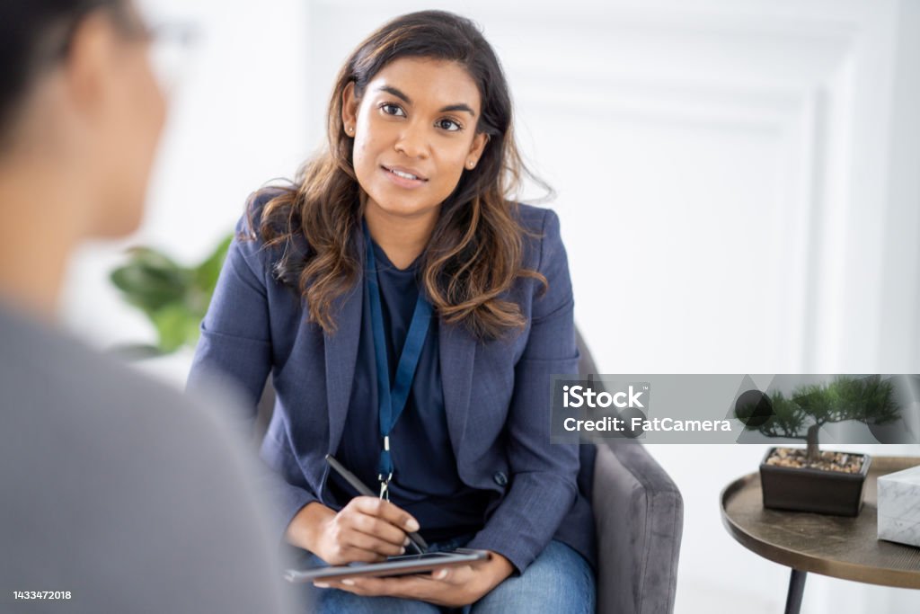 Therapy A therapist listens contemplatively while her client speaks. They are seated in a modern well lit office space. Mental Health Professional Stock Photo